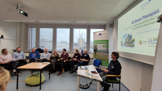 Eine Gruppe von Menschen arbeitet an einem Planspiel und sitzt gemeinsam vor einer Pr&auml;sentation