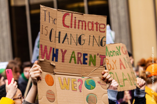 Protestierende Menschen halten ein Transparent aus Pappe hoch auf dem steht: The Climate is changing, why aren't we?