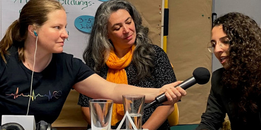 Aufnahme des Podcast im Projekt Idee und wie. Monika Konigorski interviewt eine ehrenamtliche Initiative und hält dafür einer Dame ein Mikrofon hin.