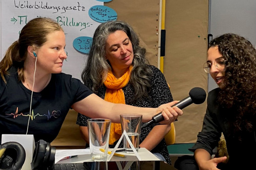 Aufnahme des Podcast im Projekt Idee und wie. Monika Konigorski interviewt eine ehrenamtliche Initiative und hält dafür einer Dame ein Mikrofon hin.