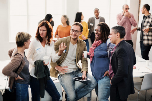 Gruppe von Menschen die freundlich miteinander diskutieren, im Hintergrund stehen drei Zweiergruppen die sich unterhalten