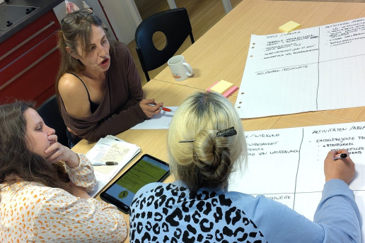 Drei Frauen sitzen um ein Blatt Papier herum an einem Tisch und diskutieren eine Idee