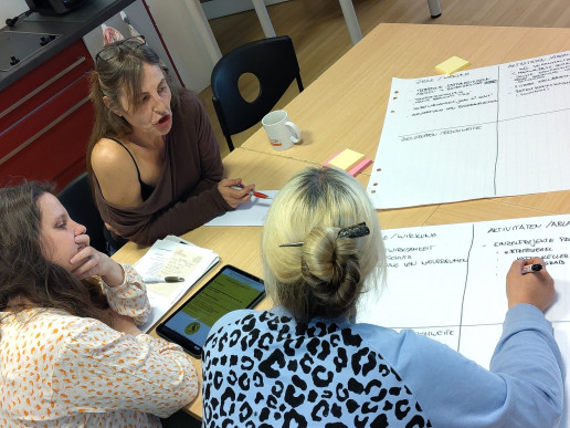 Drei Frauen sitzen um ein Blatt Papier herum an einem Tisch und diskutieren eine Idee