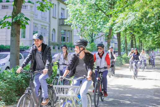 Eine Gruppe radelt durch Bonn. Entlang der Straße stehen Bäume. Foto: (c) Bundesstadt Bonn, Kolja Matzke